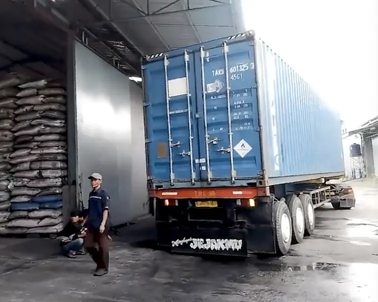 Shipping container parked at Cocobriq factory with workers finishing loading boxes of coconut charcoal briquettes